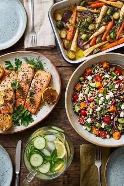 healthy dinner ideas for family , colorful spread of salmon, roasted vegetables, grain salad and water on a wooden family dinner table