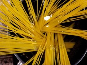 Dry spaghetti fanned across a wide pan of water on the hob, the starting point for how to cook pasta properly