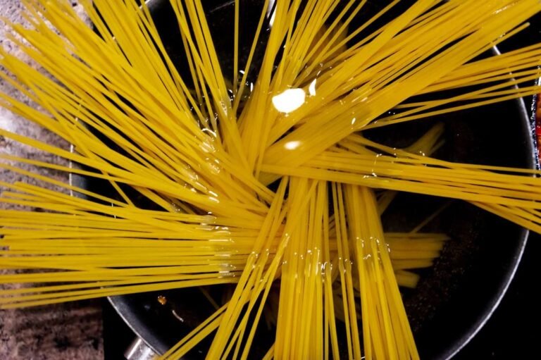 Dry spaghetti fanned across a wide pan of water on the hob, the starting point for how to cook pasta properly