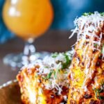 Charred Mexican street corn recipe served on the cob with grated cotija cheese, chile powder and chopped cilantro