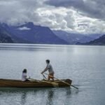 Rowing boat drink setting as a couple rows a wooden boat across a calm mountain lake