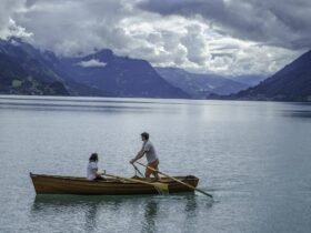 Rowing boat drink setting as a couple rows a wooden boat across a calm mountain lake