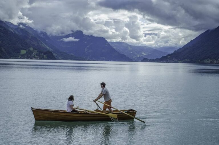Rowing boat drink setting as a couple rows a wooden boat across a calm mountain lake