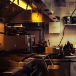 Commercial kitchen equipment checklist in practice: range under a Type I hood, prep tables, refrigerated base and a fire extinguisher in a small restaurant kitchen