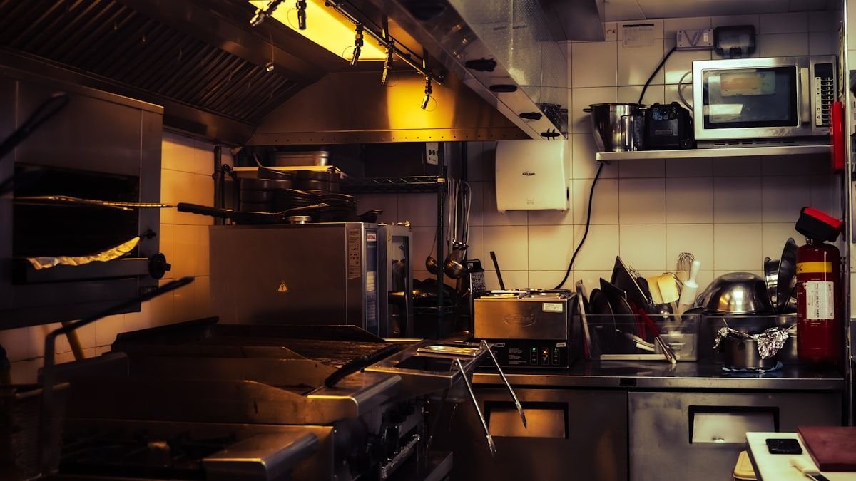 Commercial kitchen equipment checklist in practice: range under a Type I hood, prep tables, refrigerated base and a fire extinguisher in a small restaurant kitchen
