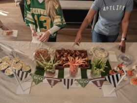 Tailgating party food ideas spread with wings, pretzel jars, popcorn cups and veggie sticks on a football themed table