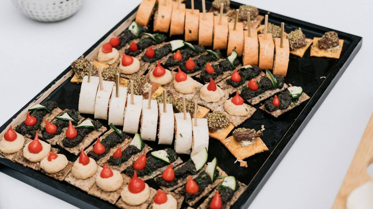 Cocktail party food ideas on one tray: canapes, pinwheels and topped crackers lined up for a standing crowd