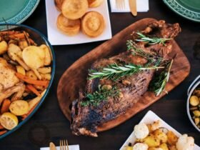 Thanksgiving side dishes spread across a dark table: rolls, roasted vegetables, Brussels sprouts and potatoes around the roast